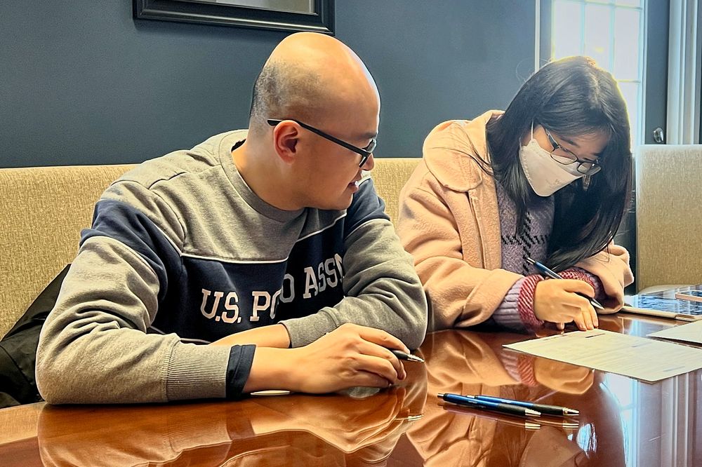 Shuai and Linwei smiling at the closing table, signing the papers for their first home